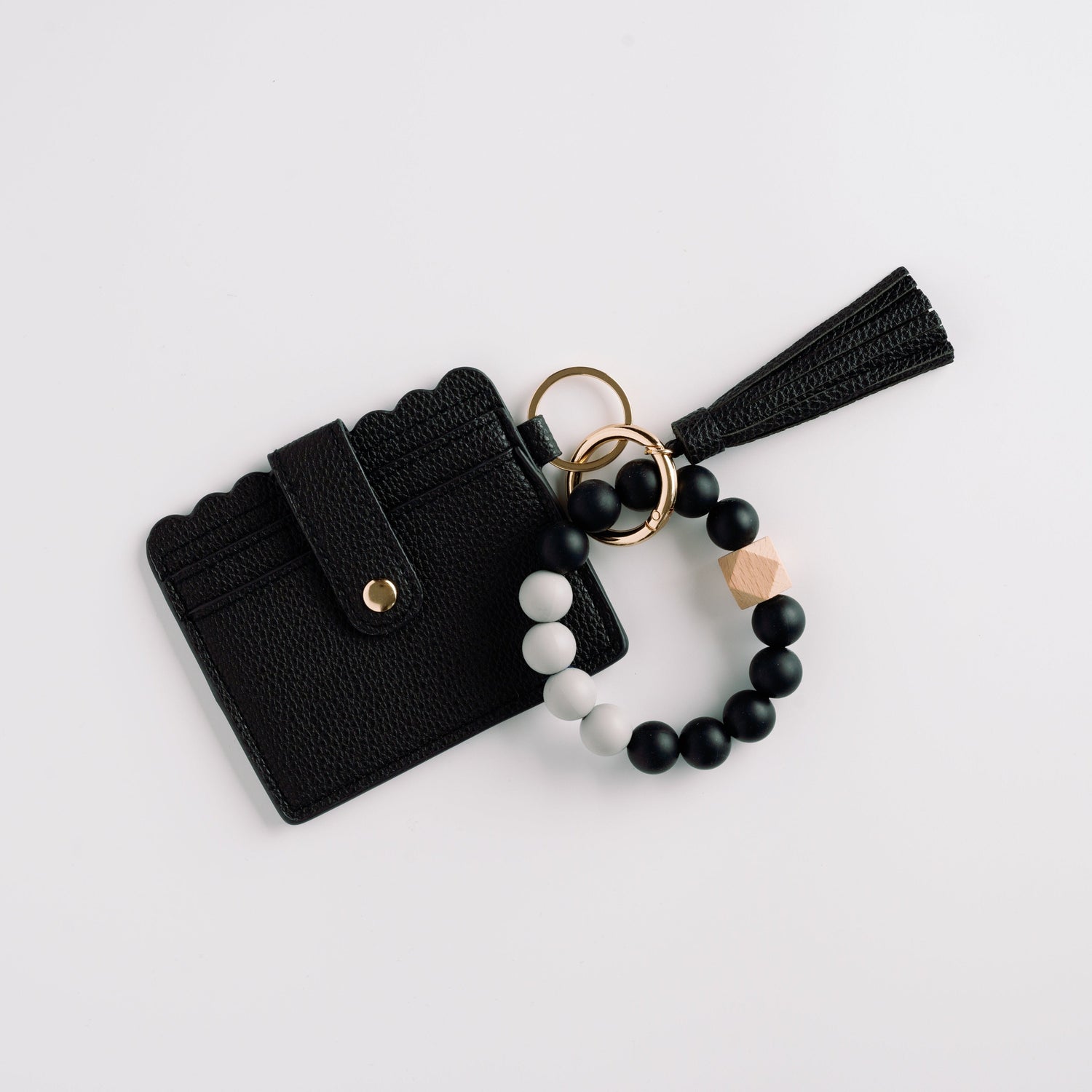 Black cardholder with scalloped edge, tassel keychain, and black and white beaded bracelet.