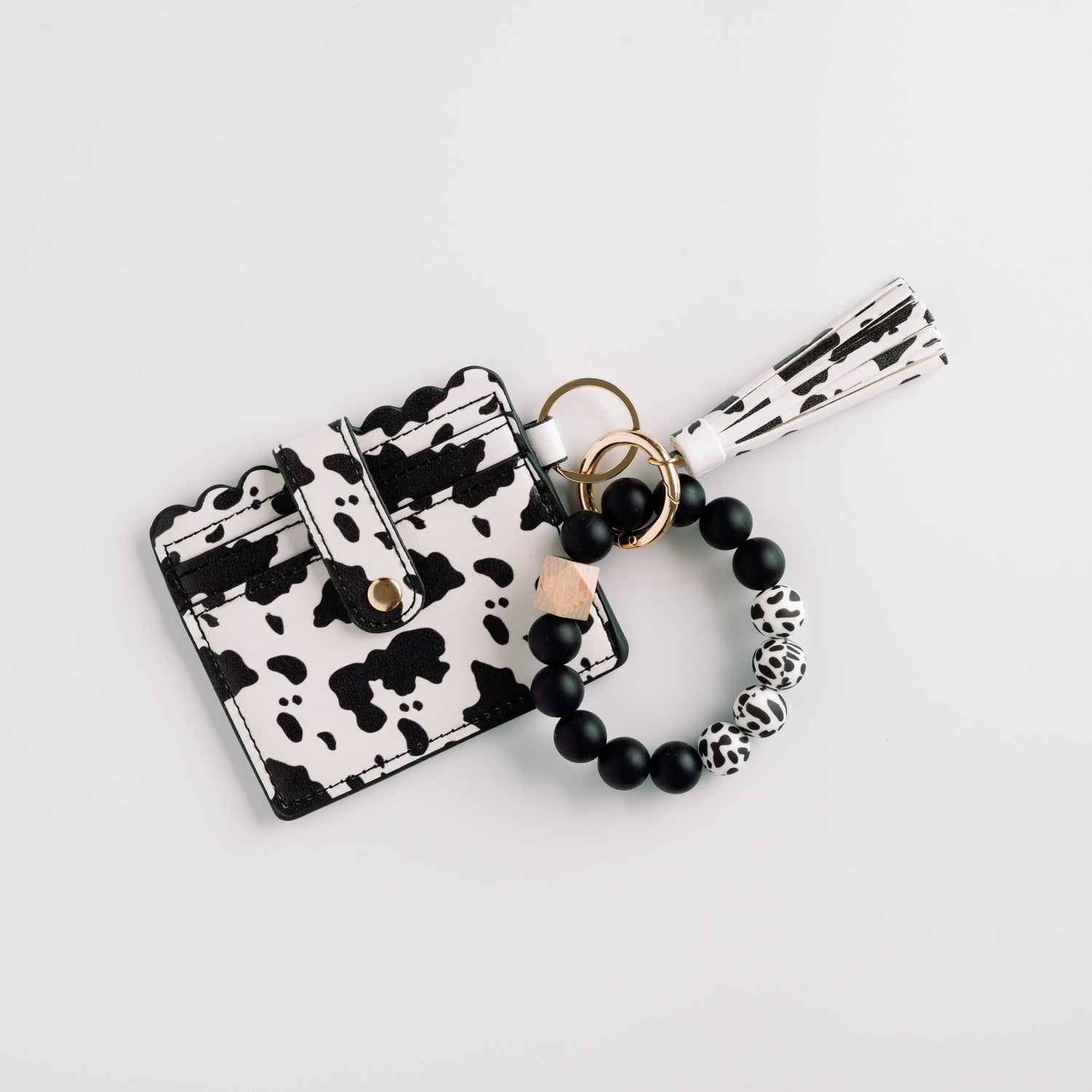 Cow-print cardholder with scalloped edges, gold button, and black bead bracelet with tassel.