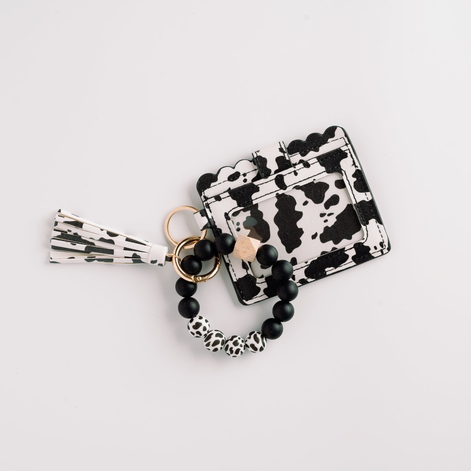 Black and white cow print wallet with beaded keychain and tassel on a white background.
