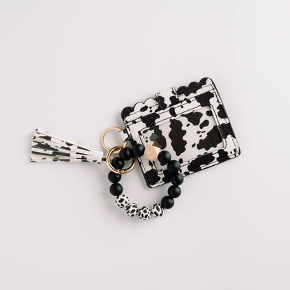 Black and white cow print wallet with beaded keychain and tassel on a white background.