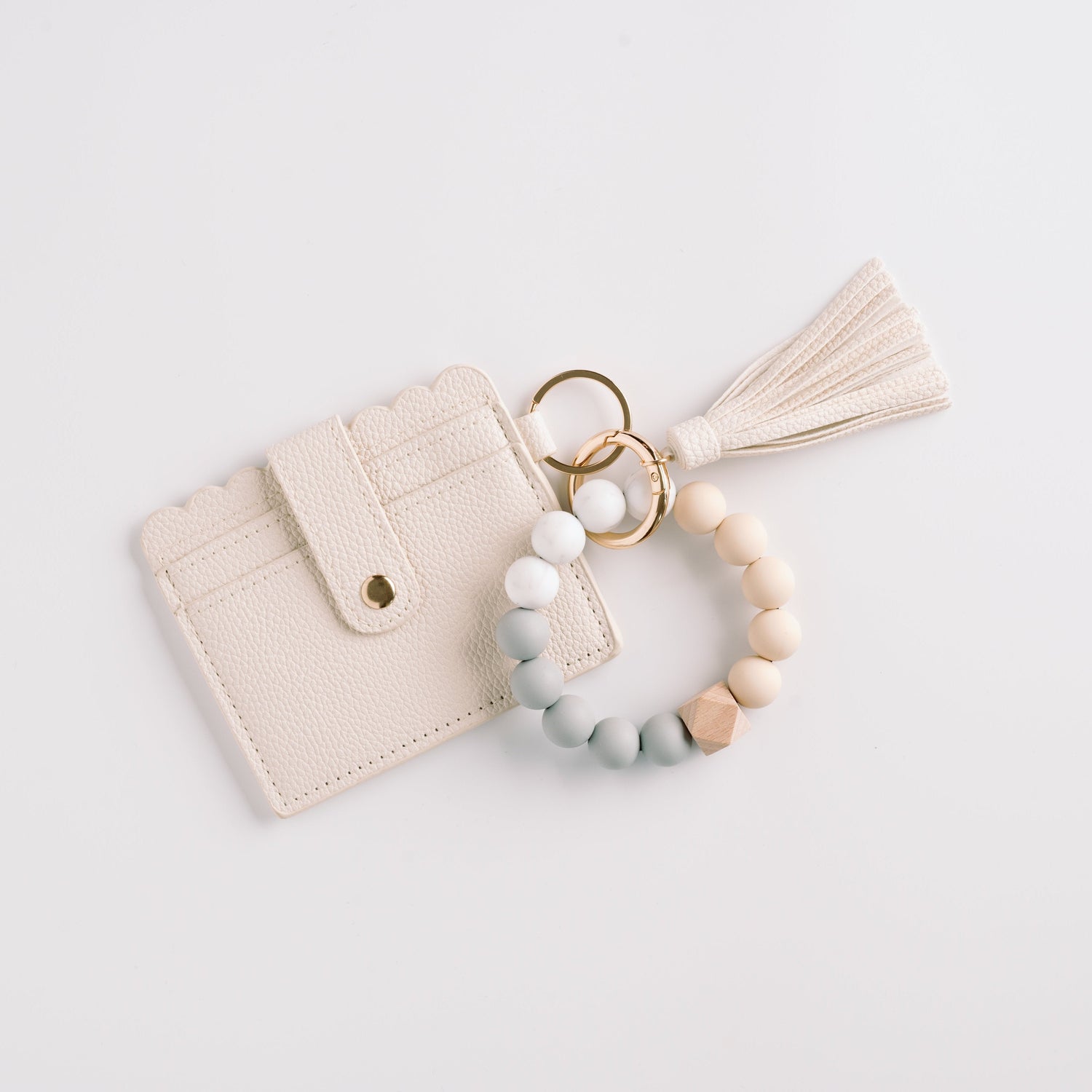 Cream cardholder with scalloped edges, tassel, and a beaded key ring in neutral tones.