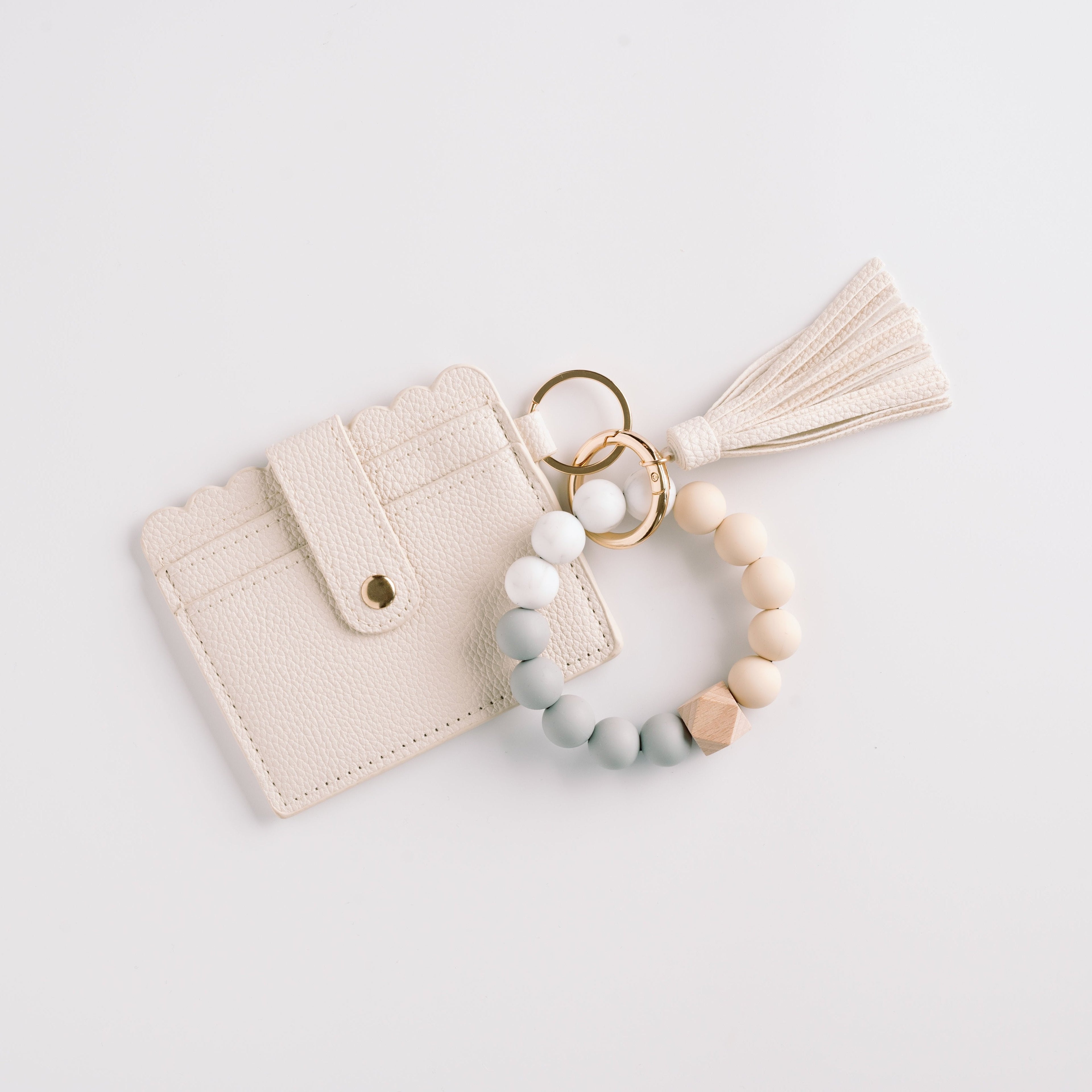 Cream cardholder with scalloped edges, tassel, and a beaded key ring in neutral tones.