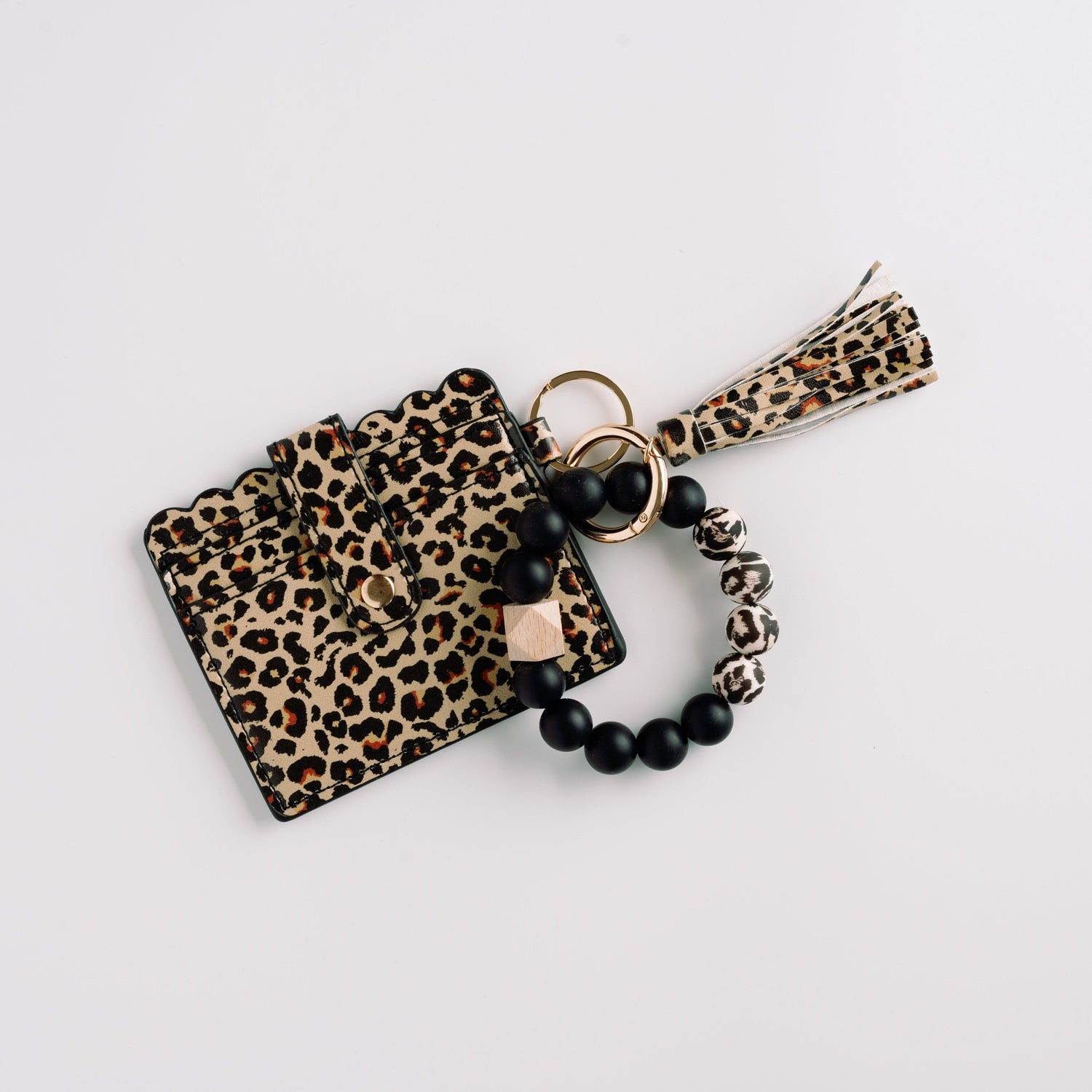 Leopard print wallet with scalloped edges, tassel, and black beaded loop keychain on white.