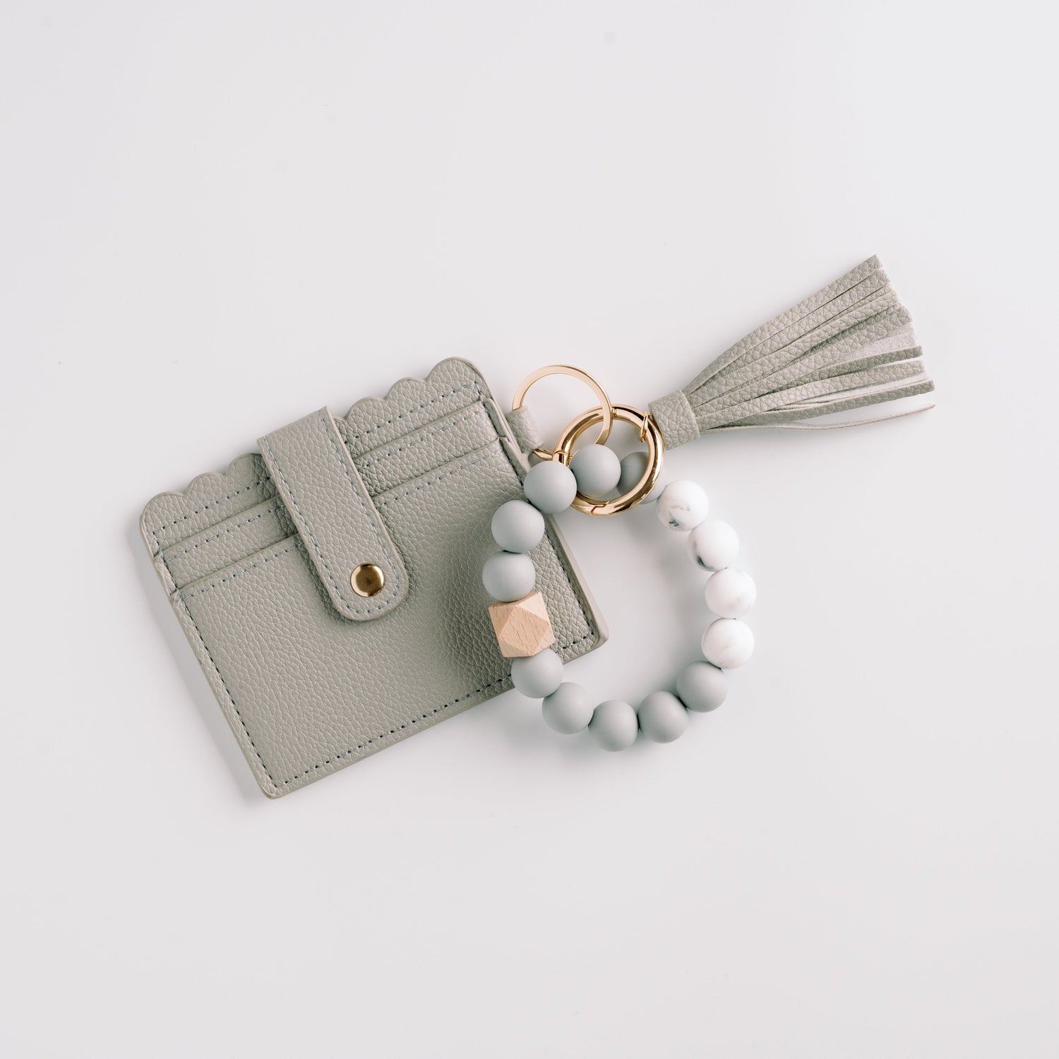 Gray cardholder with scalloped edges, gold button, tassel, and beaded wristlet on white background.