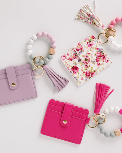 Pastel wallets with tassels and floral patterns, attached to bead keychains on a white background.
