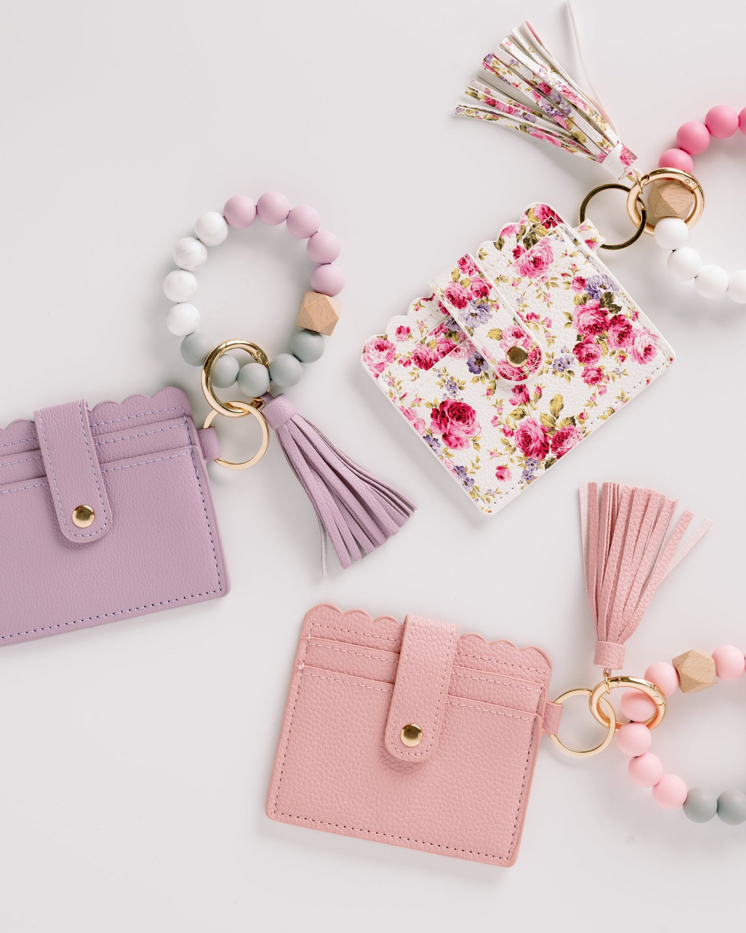 Three cardholders in pink, purple, and floral designs, each with a matching tassel and bead keychain.