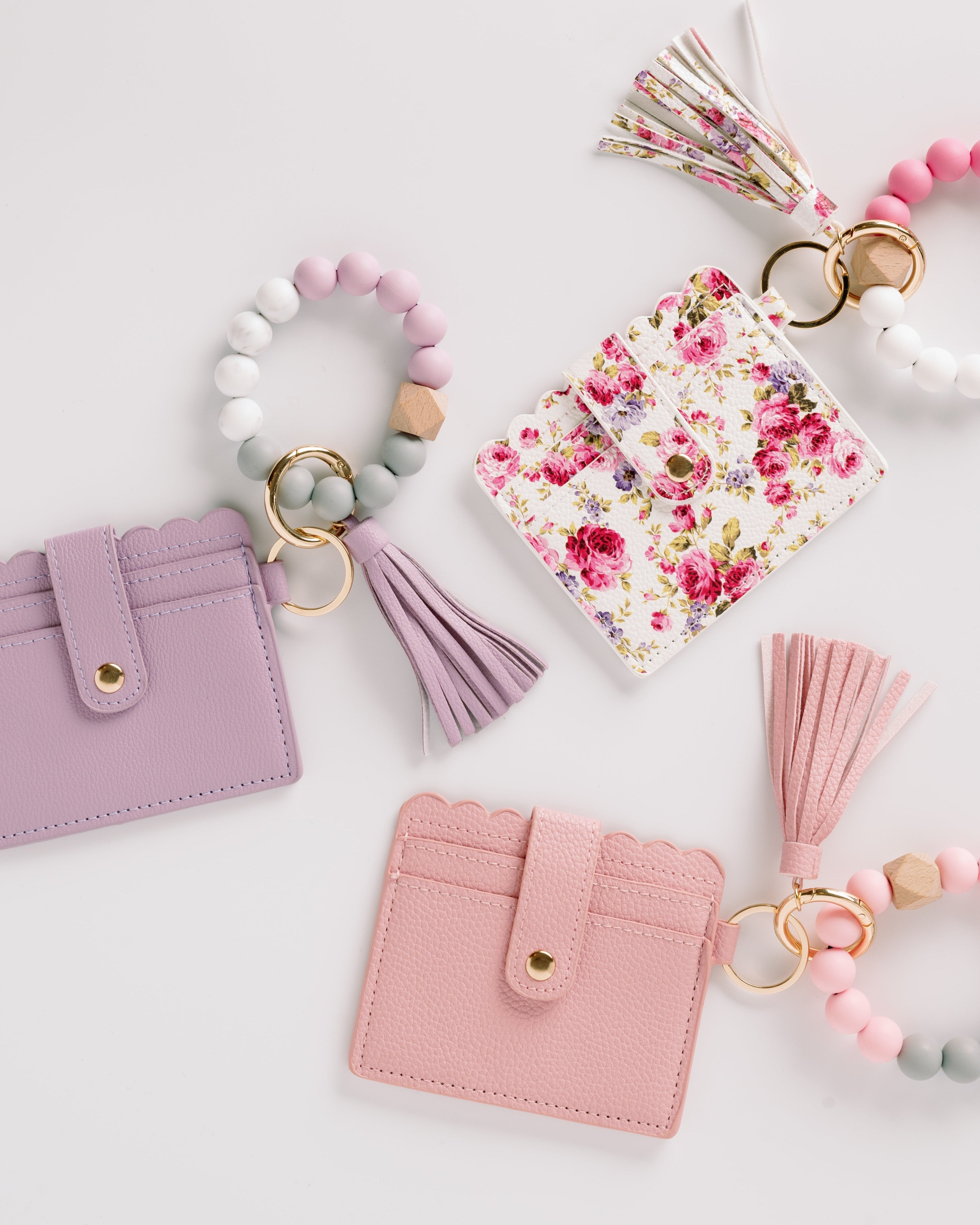 Three cardholders in pink, purple, and floral designs, each with a matching tassel and bead keychain.