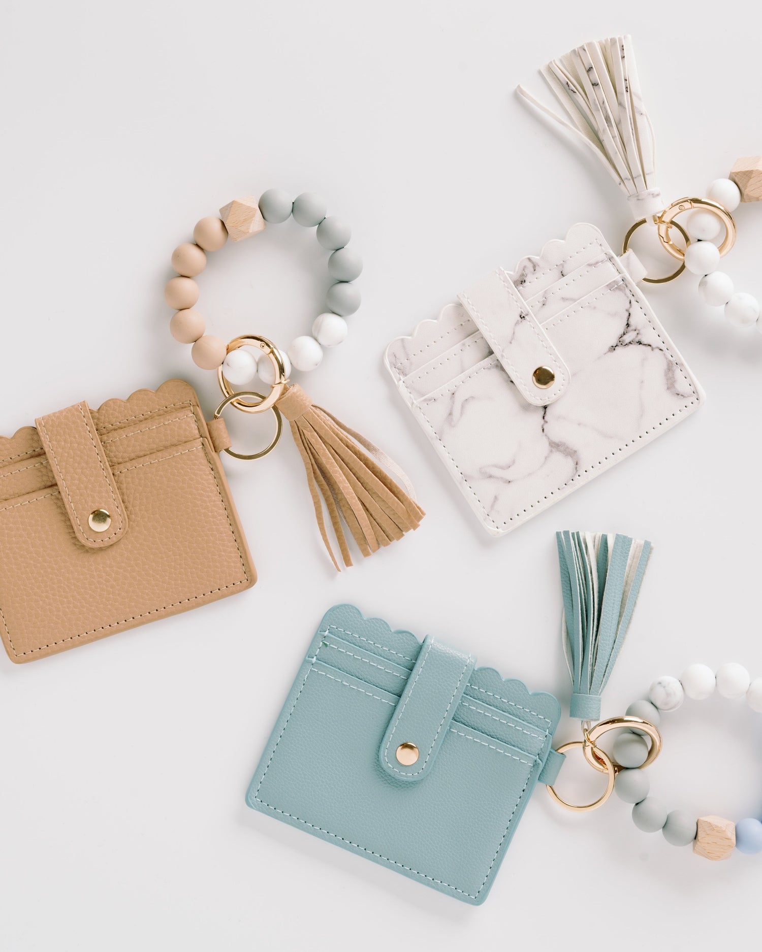 Leather card holders with tassels, wood bead keychains in beige, white, and teal on white background.