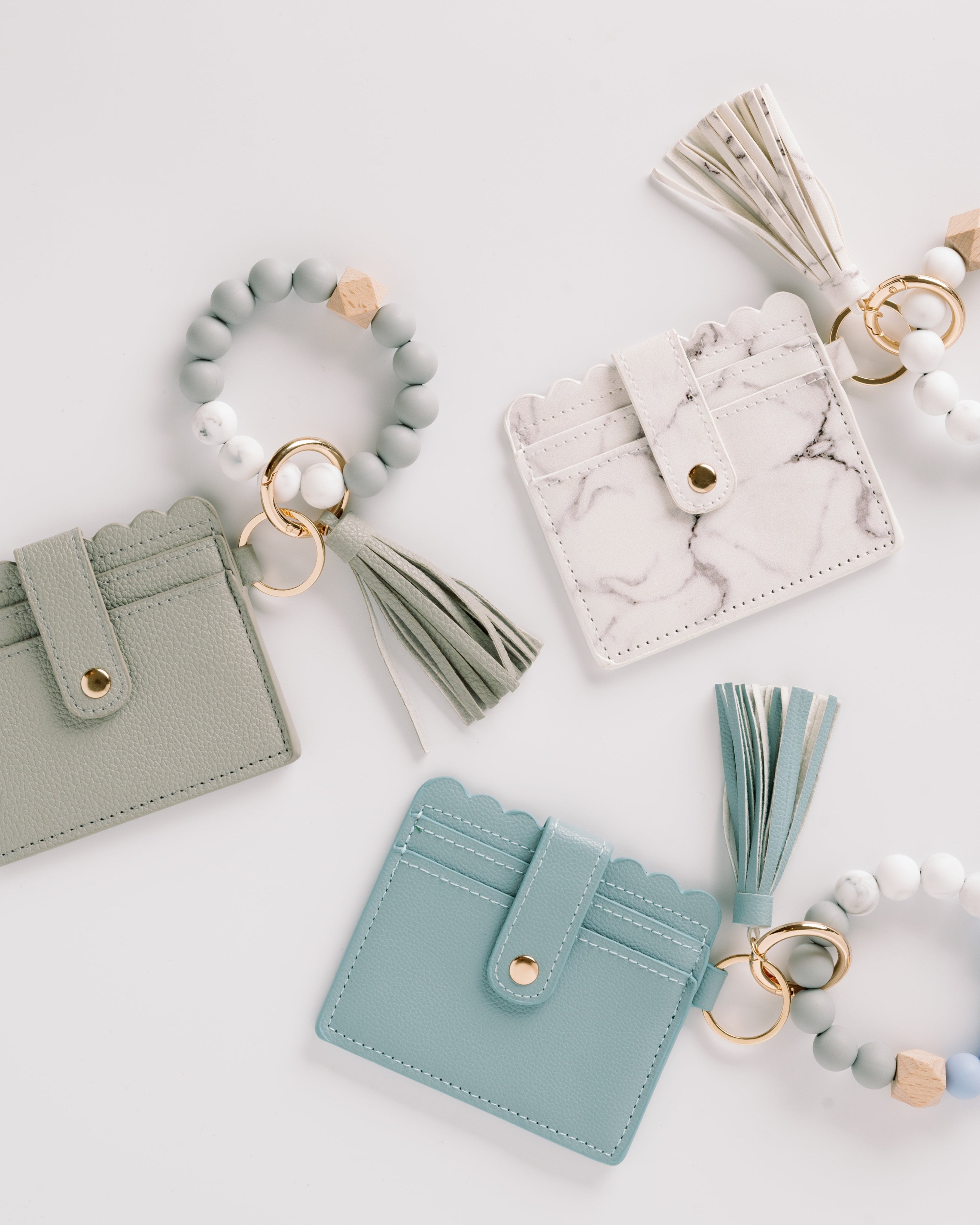 Three cardholders in green, white, and teal with tassels and beaded keyrings on a white background.
