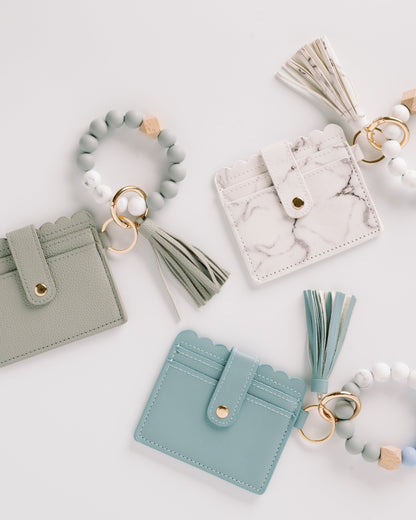 Three cardholders in green, white, and teal with tassels and beaded keyrings on a white background.