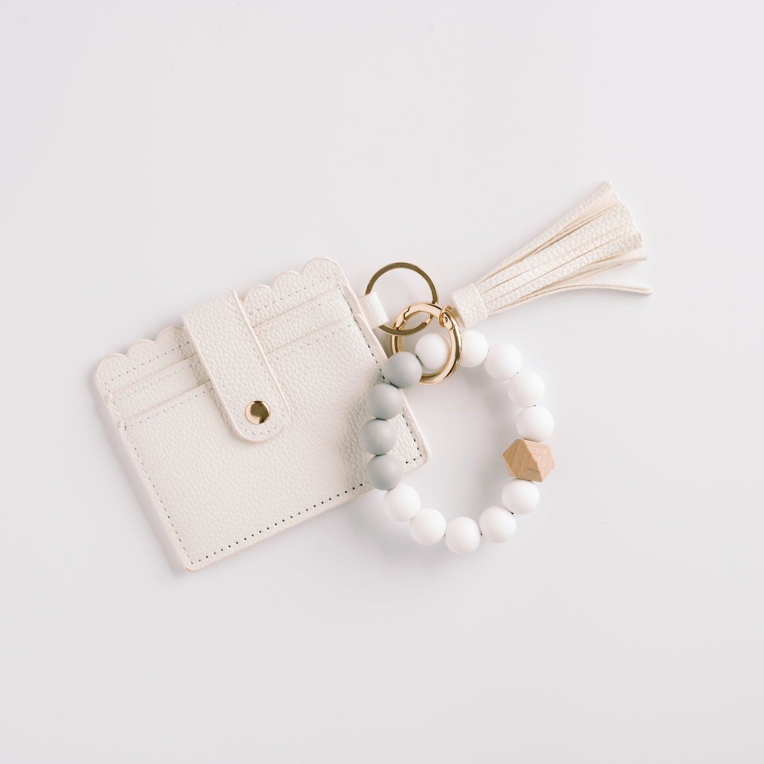 White cardholder with scalloped edges, beaded keychain, gold rings, and tassel on white background.