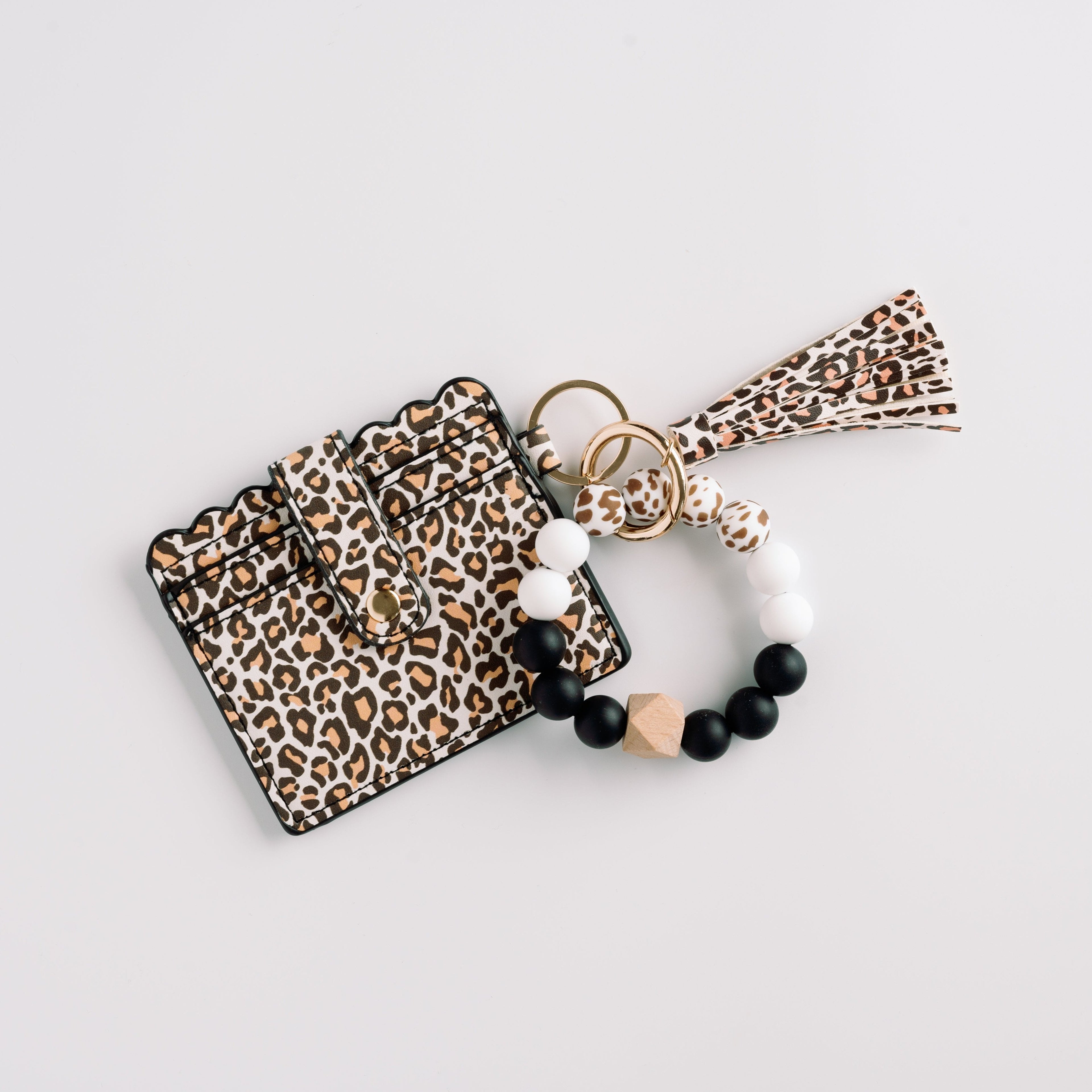Leopard-print wallet with tassel and bead bracelet in black, white, and wood on light background.