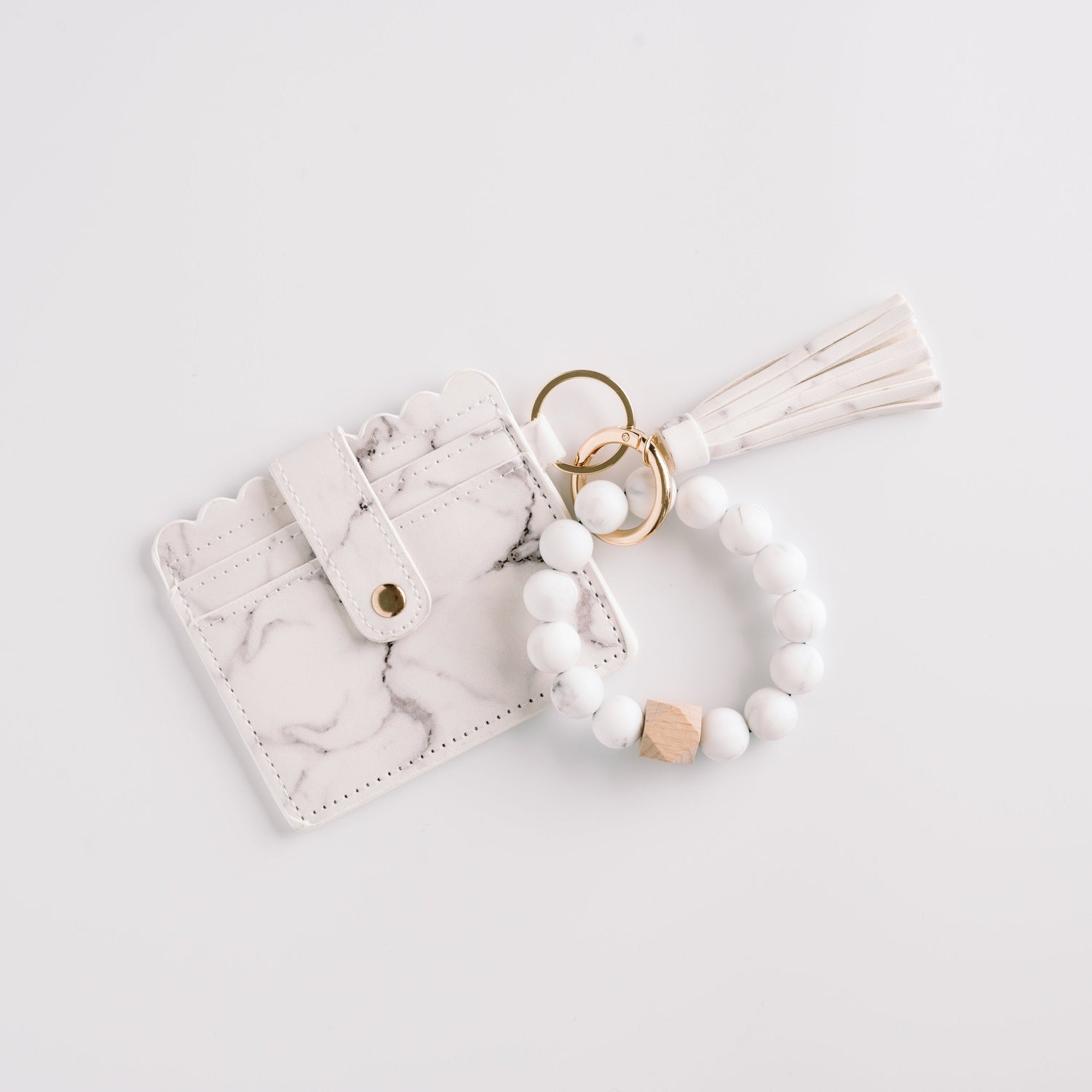 White marble cardholder with tassel, gold ring, and beaded bracelet on a light gray background.
