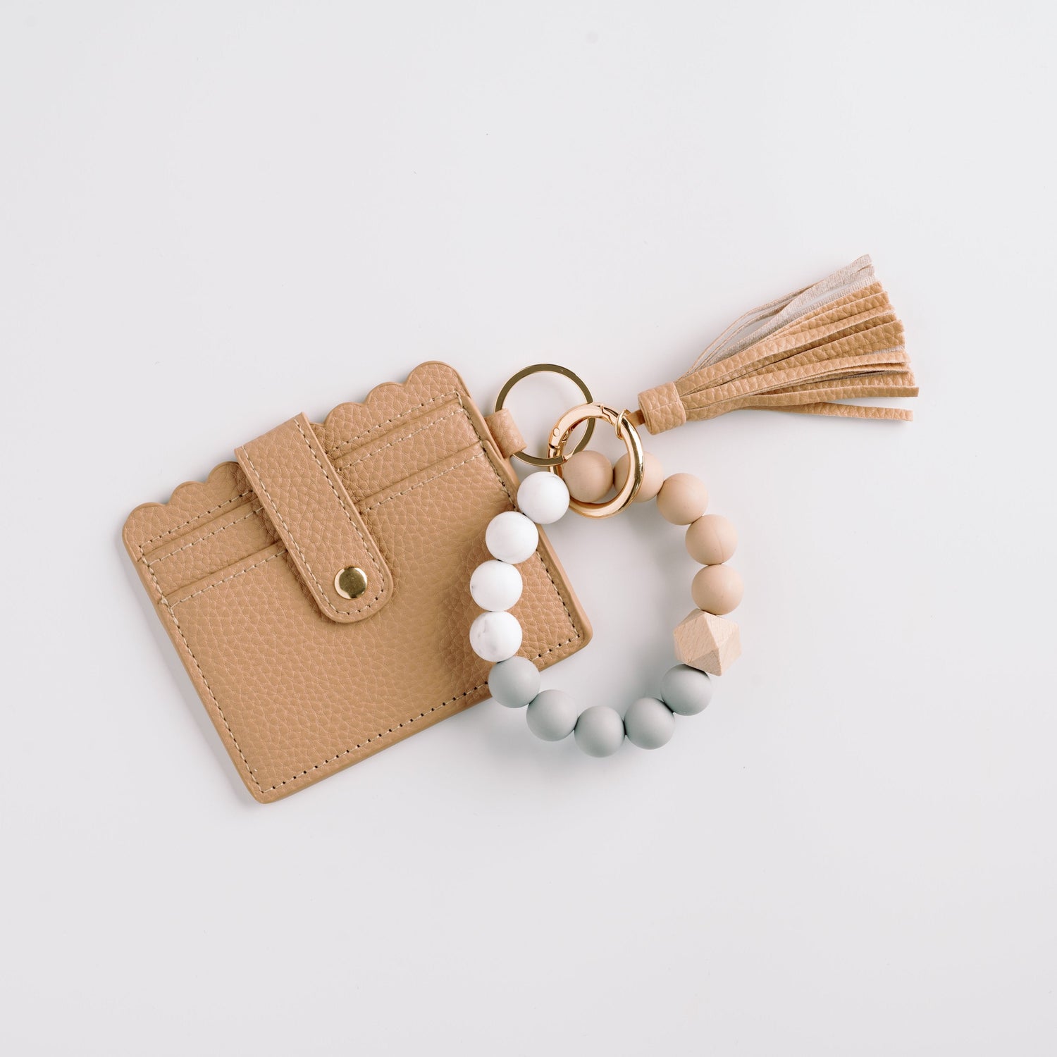 Tan scalloped wallet with a tassel and a beaded bracelet keychain in muted tones on a white background.