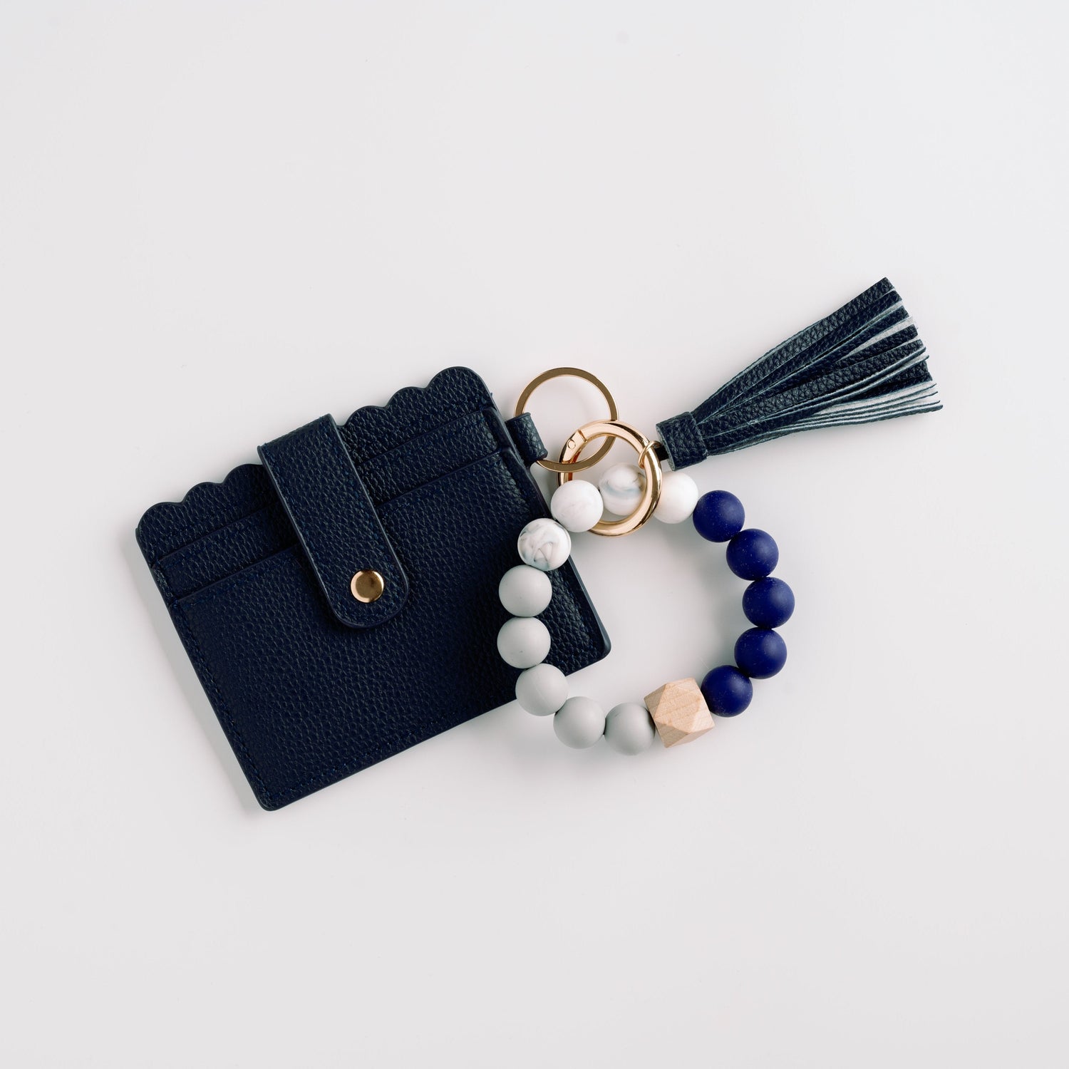 Navy cardholder with scalloped edge, blue-white beaded bracelet, and tassel keychain.