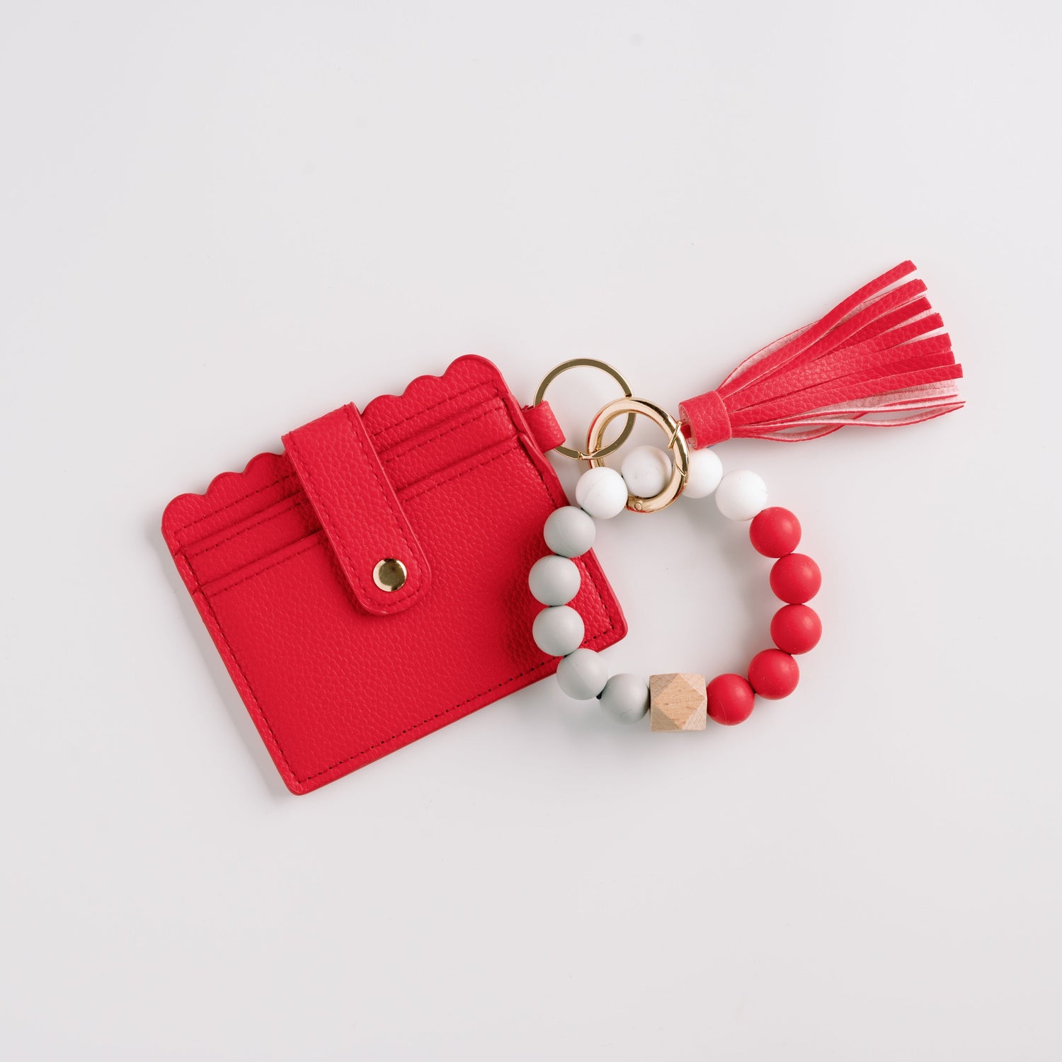 Red cardholder with scalloped edge, attached beaded keychain, and red tassel on white background.