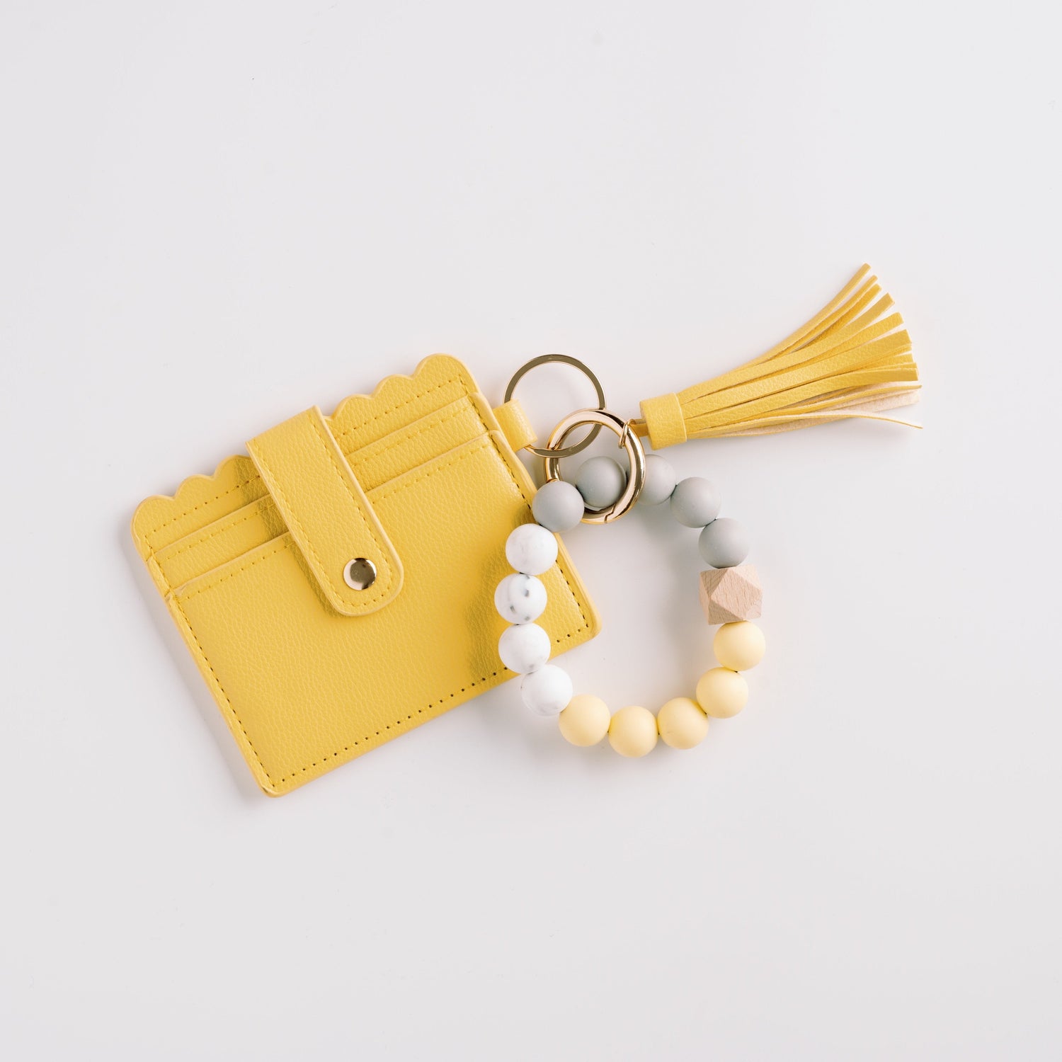 Yellow cardholder with scalloped edge, tassel, and bead bracelet in grey, yellow, and beige.