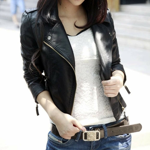 Woman in a black leather jacket and white lace top, holding a belt on blue jeans.